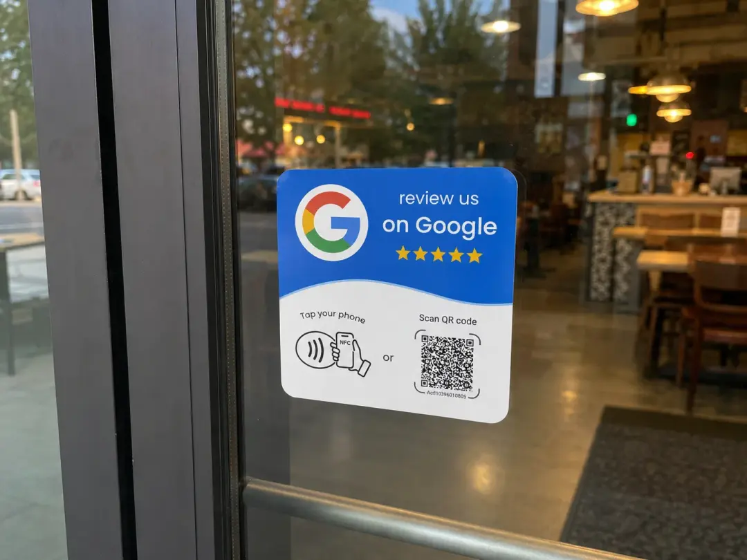 The same review card stuck on a shop door, with the NFC tap symbol and QR code facing customers as they leave.